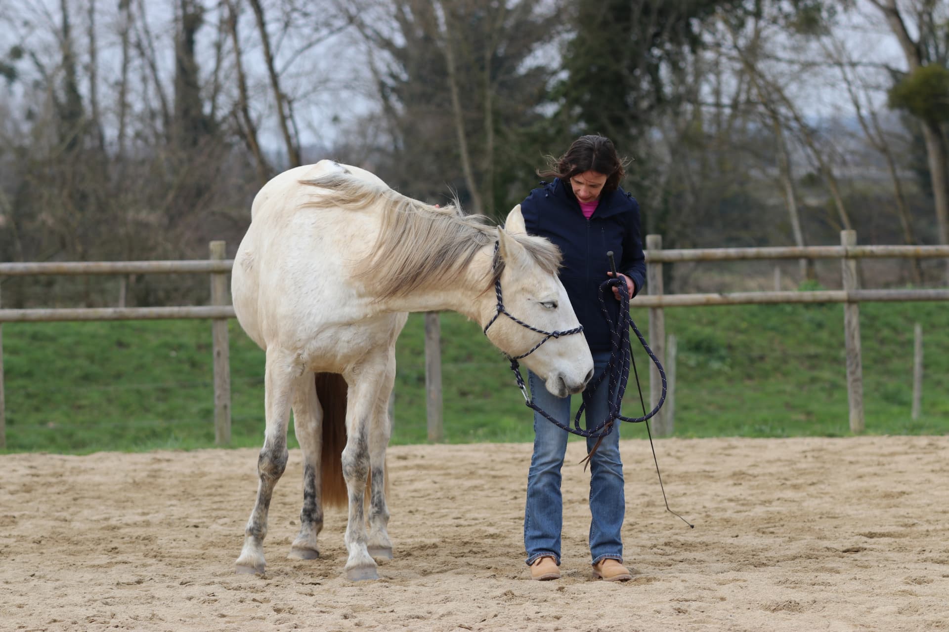Adeline Gourdon marchant à pied aux côtés d’un cheval blanc dans une carrière de sable