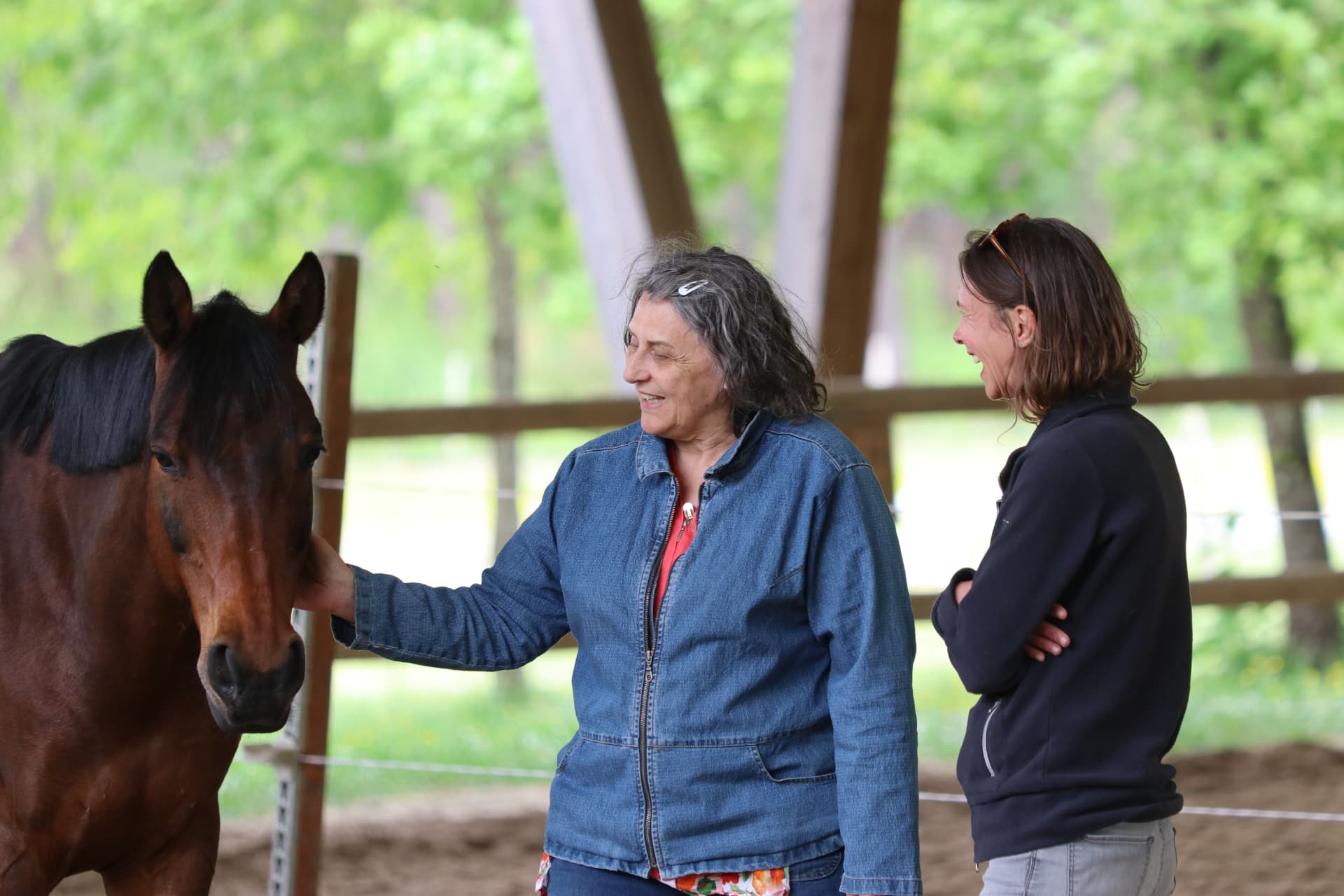 Participante caressant un cheval, accompagnée par Adeline Gourdon, équicoach, souriante à ses côtés